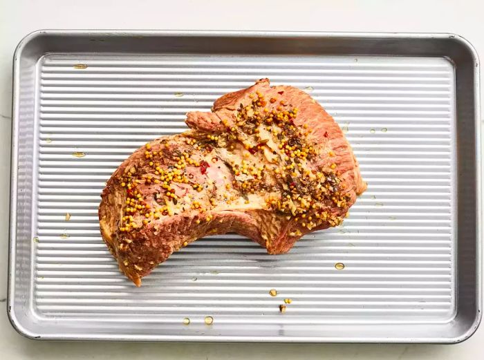 A cooked brisket resting on a baking sheet, coated in spices.