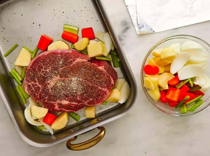 A top-down view of sliced vegetables arranged around a roast in a baking pan.