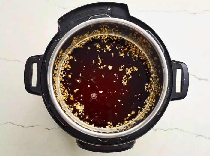 A top-down view of a pressure cooker filled with a flavorful marinade.