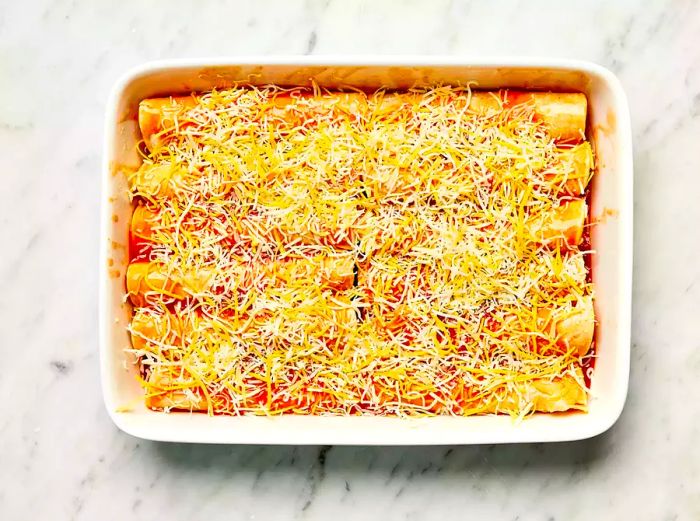 Refried Bean and Cheese Enchiladas topped with melted cheese in a white casserole dish