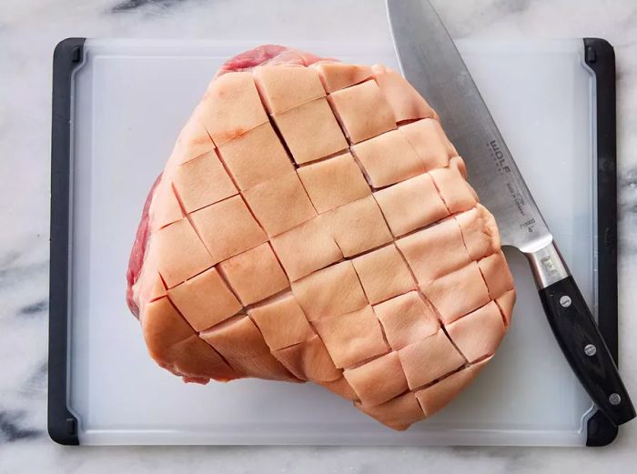 Top-down view of a ham being scored with a knife on a cutting board.