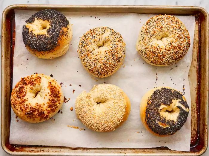 Freshly baked bagels with toppings on a baking sheet