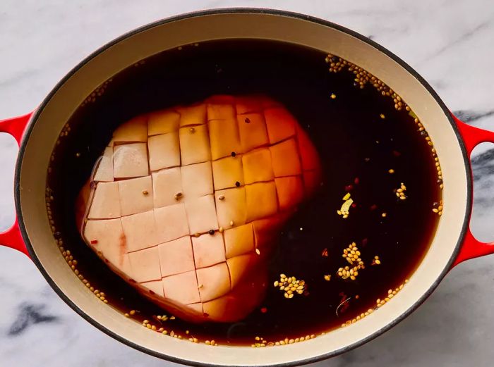 Top-down view of a roast soaking in brine inside a large cooking pot.