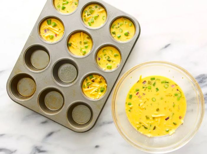 A top-down view of the frittata mixture being poured into a muffin tin.