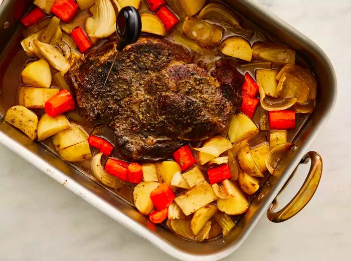 The baked roast rests in a baking dish, surrounded by an assortment of chopped vegetables.