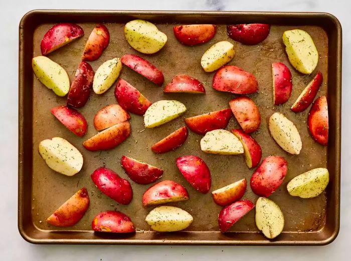 Cut and seasoned potatoes spread evenly on a baking tray.