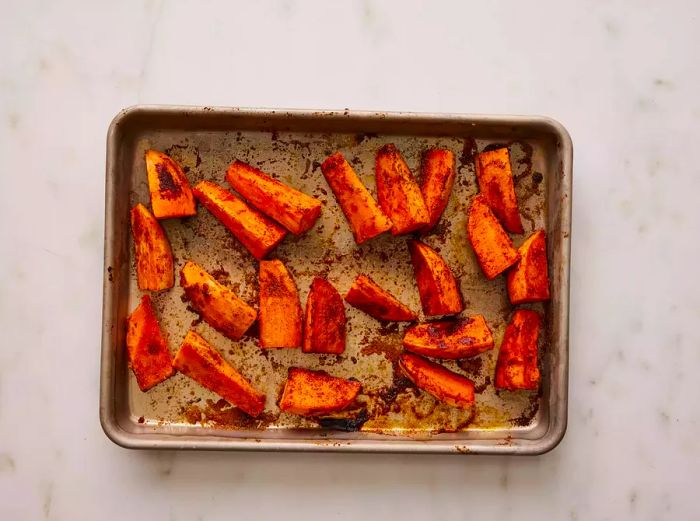 A baking pan filled with golden-brown baked sweet potato wedges, coated in seasoning.