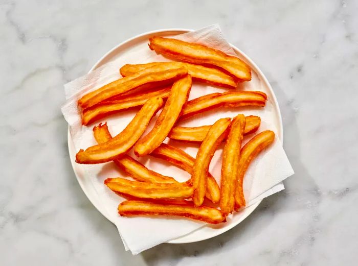 A plate lined with paper towels, holding pieces of freshly fried churros.