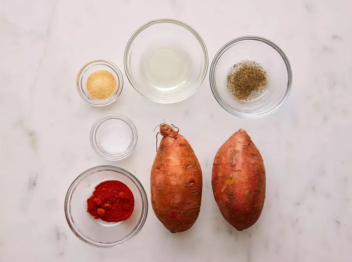 A top-down view of two sweet potatoes, along with salt, pepper, garlic powder, and paprika.