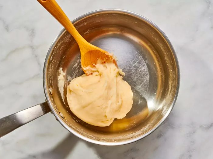 A small pot filled with dough and a wooden spoon.