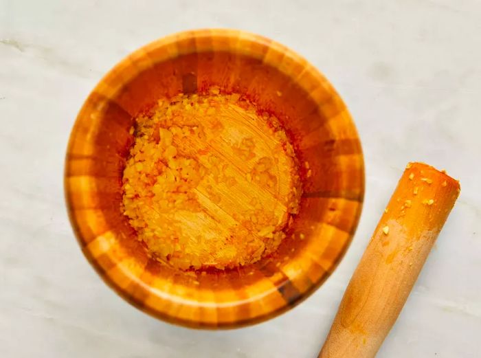 Top-down view of garlic being crushed in a wooden mortar with a pestle