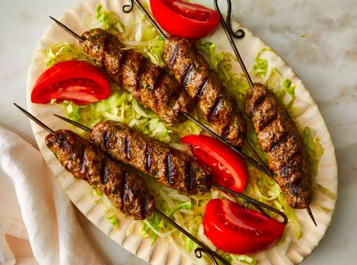 Overhead shot of a plate filled with kofta kebabs, garnished with lettuce and tomatoes.