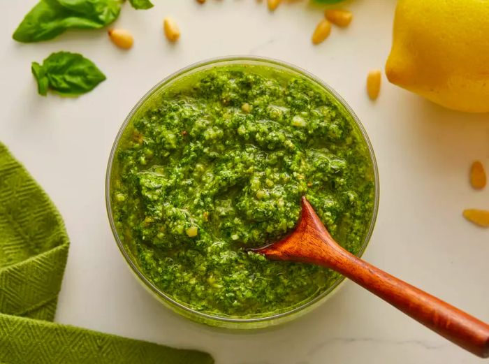 Looking down at a bowl of spinach basil pesto with a wooden spoon resting on top