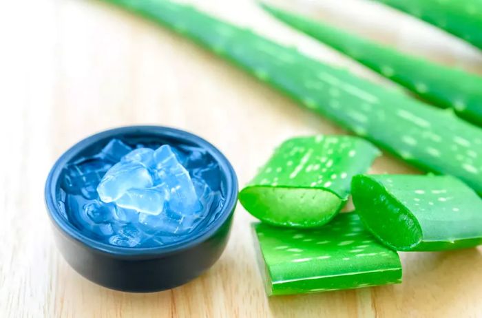 A bowl of aloe vera juice accompanied by fresh aloe vera leaves on a wooden surface