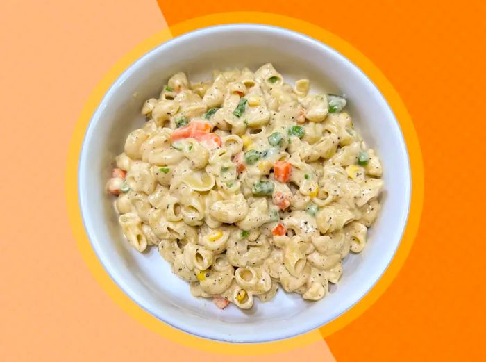 A bowl of smoked gouda mac and cheese with vegetables on a peach-colored background