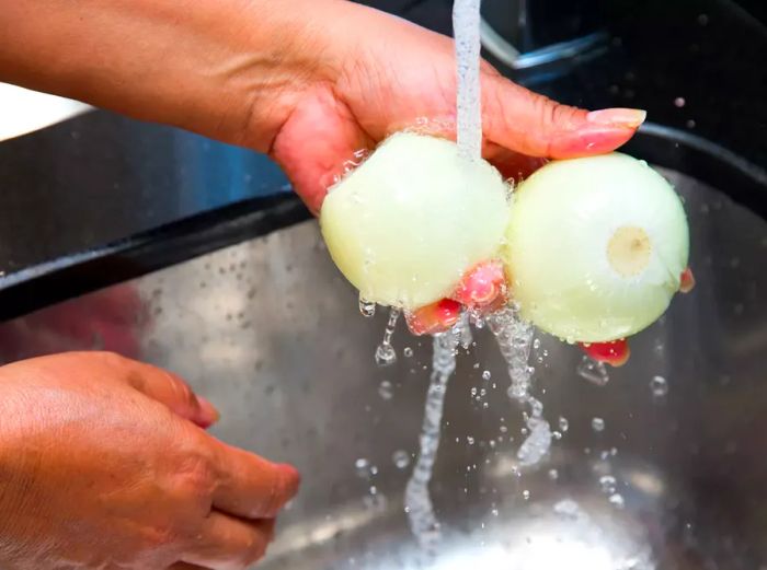 A person rinsing two white onions under running water