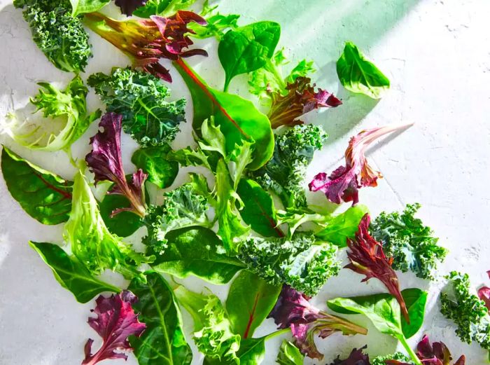 A mix of fresh salad greens arranged on a white, natural surface.