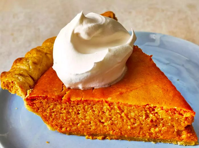 A close-up, low-angle shot of a perfectly sliced pumpkin pie topped with a dollop of whipped cream.