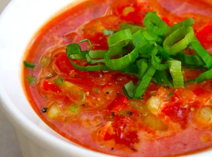 A close-up shot of a ramekin of Chef John's Gazpacho garnished with slices of green onion tops