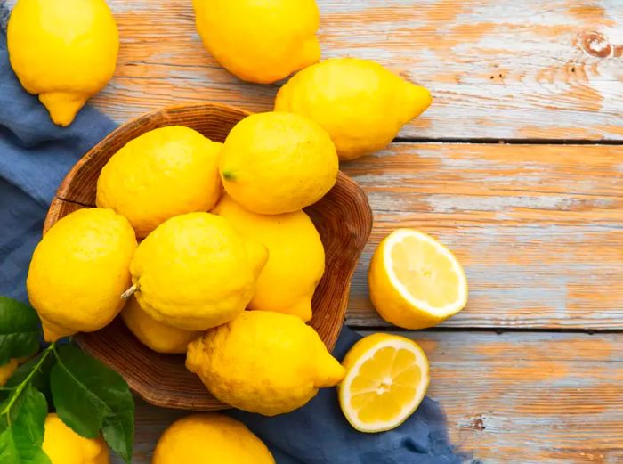 A top-down view of lemons placed in a wooden bowl on a rustic table.