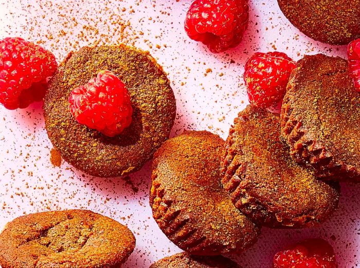 A batch of air fryer raspberry brownie bites, with a few fresh raspberries scattered on top, resting on a soft pink surface.