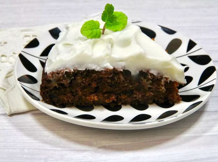 A slice of tomato soup cake topped with white frosting and garnished with a sprig of mint