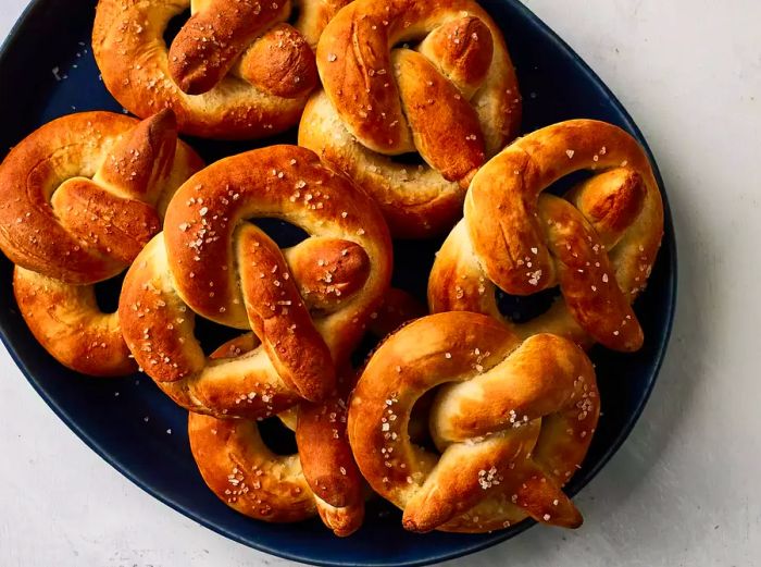 A close-up of a black platter stacked with buttery, salt-coated soft pretzels.