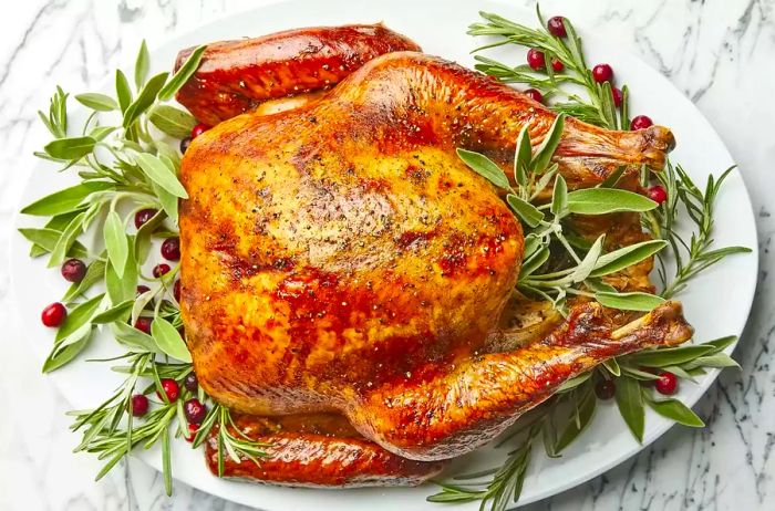 An overhead shot of a perfectly roasted turkey on a platter, garnished with fresh herbs.