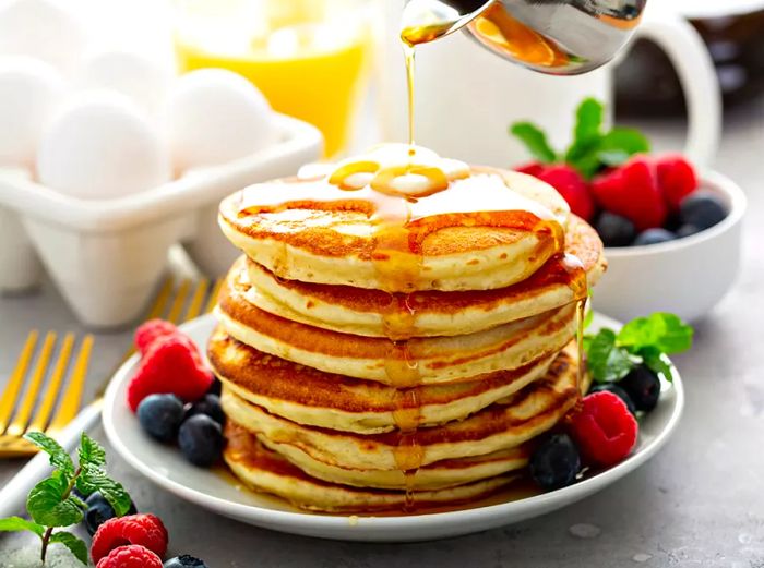 a stack of fluffy pancakes with syrup being drizzled on top