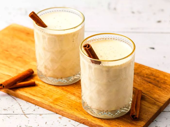 Two glasses of eggnog resting on a wooden surface.