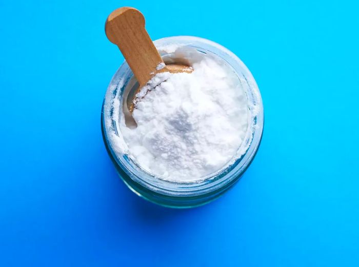 A high-angle shot of a spoonful of baking soda on a blue background.