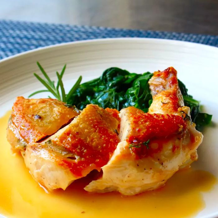 A close-up shot of sliced Airline Chicken Breast served with spinach on a white plate