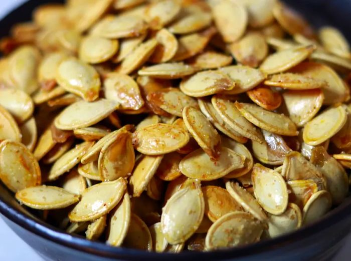 A close-up shot of roasted salted pumpkin seeds in a sleek black bowl.