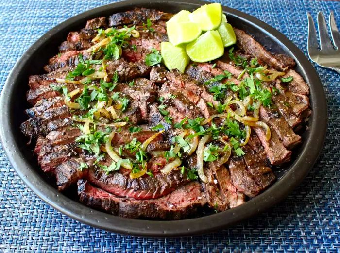 Sliced flank steak topped with caramelized onions and chopped cilantro, served with lime wedges