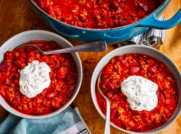 A high-angle shot of two bowls of the best damn chili, each topped with a generous dollop of sour cream.