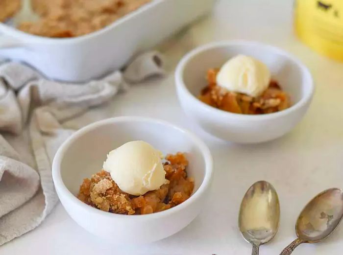 Apple crumble served in two bowls, topped with ice cream.