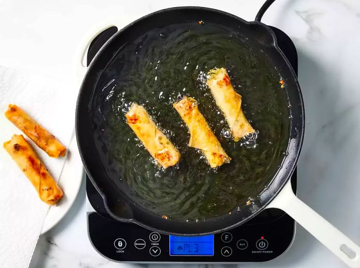 Lumpia frying in hot oil, turning golden and crisp.