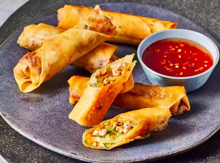 A plate of Filipino lumpia, one cut open to reveal the savory filling inside.