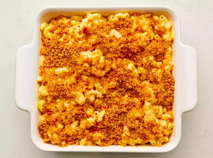 A baking dish filled with elbow macaroni in creamy cheese sauce, topped with golden breadcrumbs and a sprinkle of paprika.