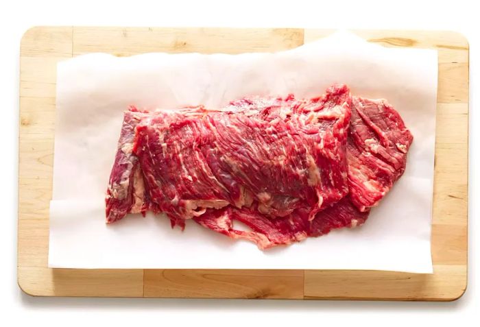 Raw skirt steak resting on parchment paper atop a wooden surface