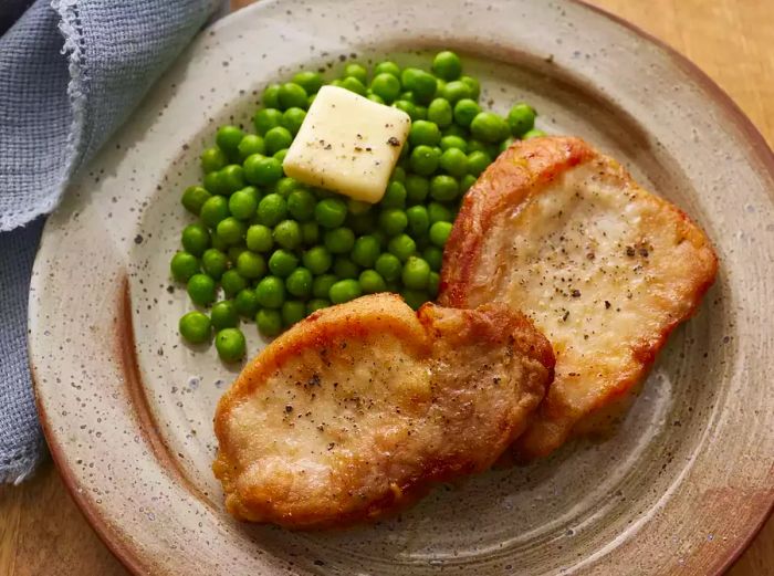 A plate of crispy golden fried pork chops paired with a side of green peas.