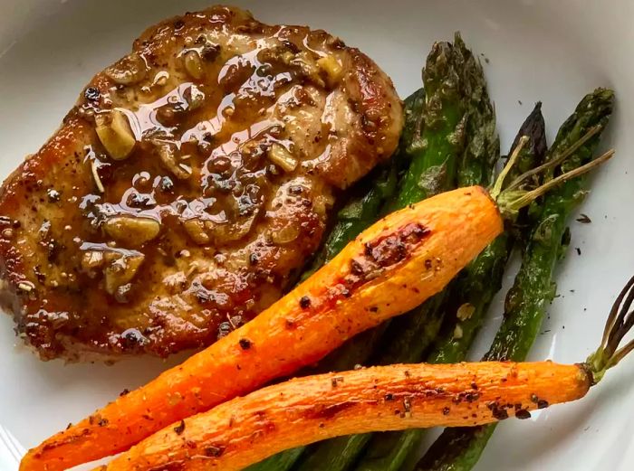 Close-up of a Modenese Pork Chop served with carrots and asparagus in a white bowl