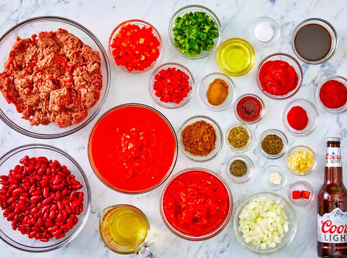 A bird's-eye view of various chili ingredients arranged in different sizes of glass bowls.