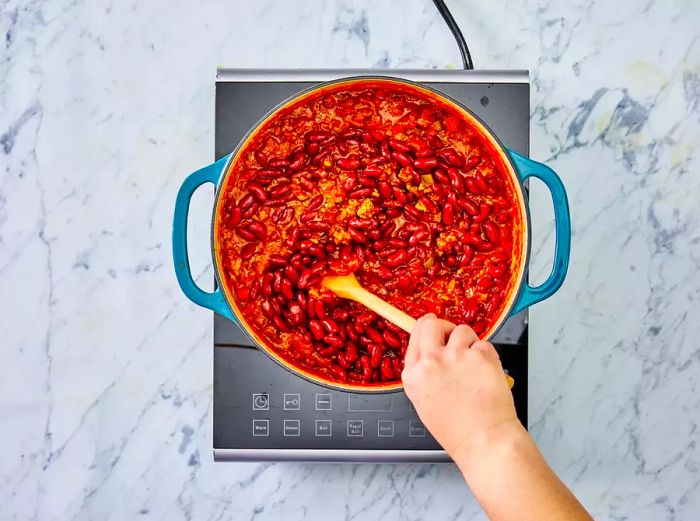 A top-down view of chili with kidney beans being stirred in.