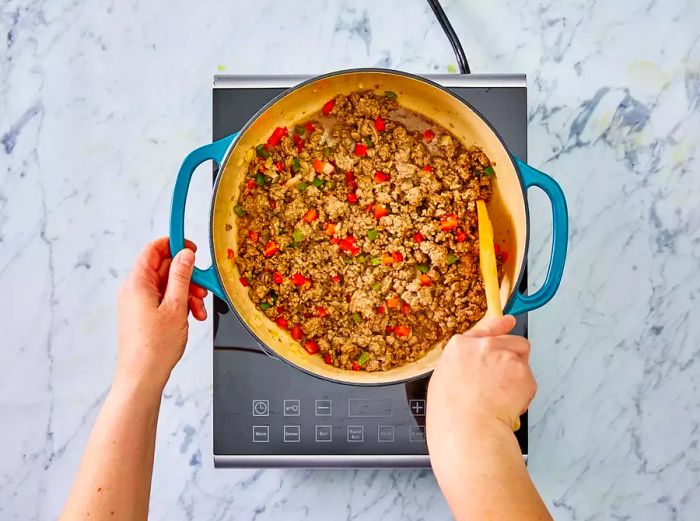 A bird's-eye view of the ground beef mixture and pepper mixture being stirred together in a skillet.