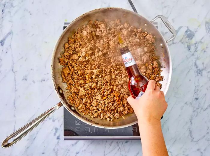 Beer being poured into the skillet with cooking ground beef.