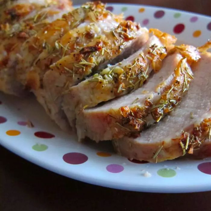 An herb-crusted pork loin served on a polka-dotted platter, beautifully sliced and plated.