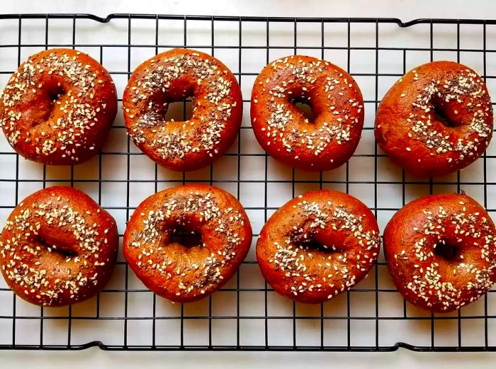 Close-up of pumpernickel bagels topped with sesame and chia seeds, resting on a cooling rack.