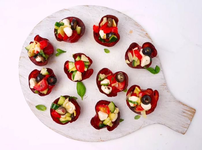 Overhead view of a round white wooden platter featuring Italian salami cup appetizers