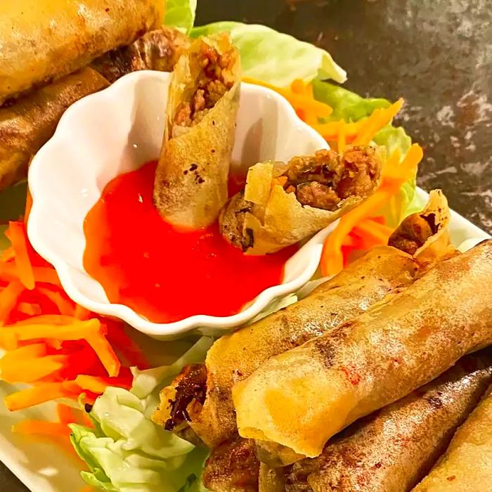 A close-up shot of classic Filipino lumpia served with sauce and fresh vegetables on a platter.